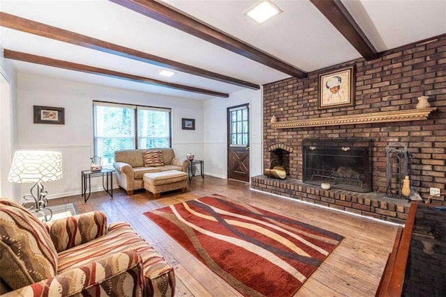 living area featuring hardwood / wood-style floors, a brick fireplace, beamed ceiling, and baseboards