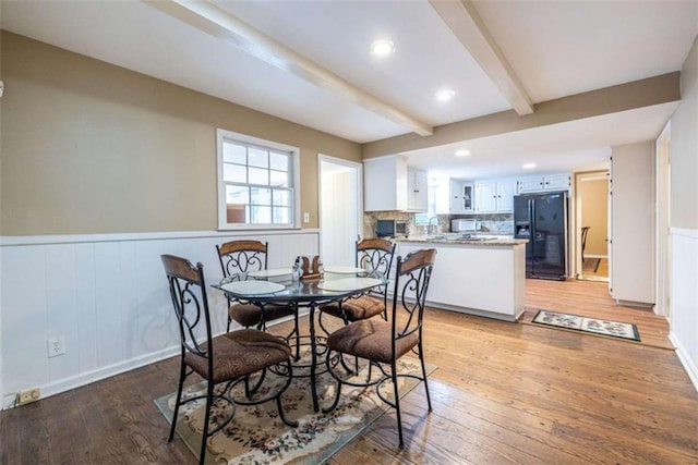 dining space with beamed ceiling, light wood finished floors, a wainscoted wall, and recessed lighting