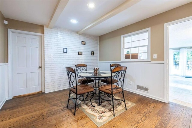 dining area featuring beam ceiling, wainscoting, wood finished floors, and brick wall
