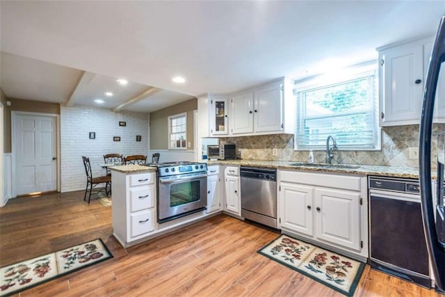 kitchen with appliances with stainless steel finishes, a sink, a peninsula, white cabinetry, and recessed lighting