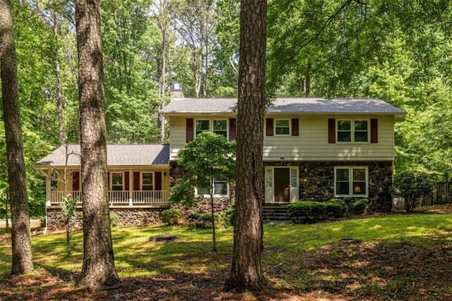 view of front facade with a chimney, stone siding, a front lawn, and covered porch
