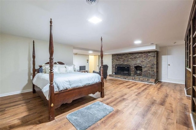 bedroom with a brick fireplace, wood finished floors, and baseboards