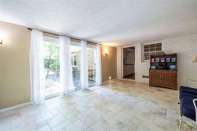 unfurnished living room featuring a textured ceiling, baseboards, light stone finish flooring, and brick wall