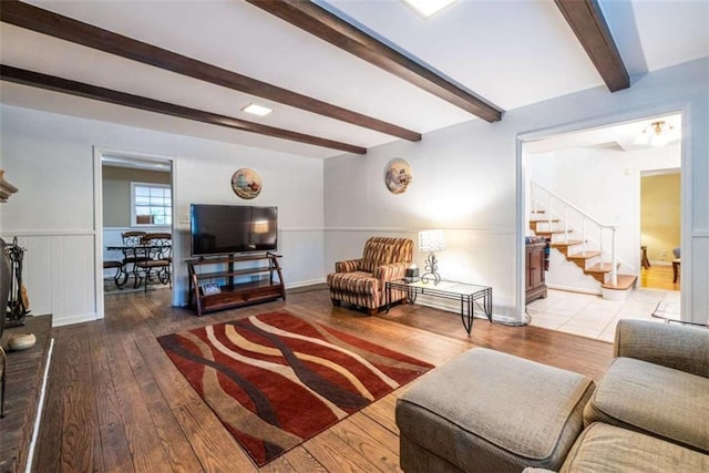 living room with beamed ceiling, stairway, wood-type flooring, and a wainscoted wall