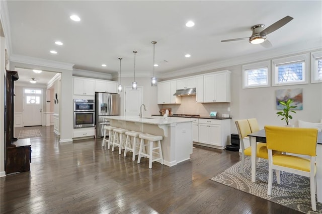 kitchen with under cabinet range hood, stainless steel appliances, dark wood-style flooring, a kitchen breakfast bar, and backsplash