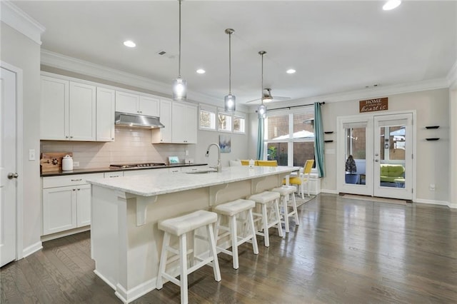 kitchen featuring decorative backsplash, dark wood-style floors, crown molding, stainless steel cooktop, and under cabinet range hood