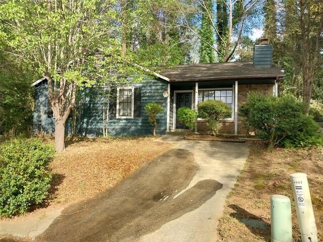 view of front of home with driveway, a chimney, and brick siding