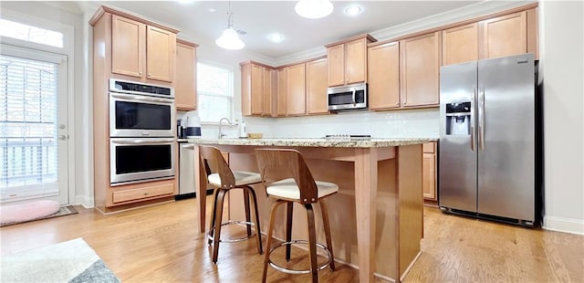 kitchen with appliances with stainless steel finishes, a center island, pendant lighting, light hardwood / wood-style floors, and light brown cabinetry