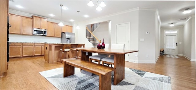 kitchen with appliances with stainless steel finishes, hanging light fixtures, light hardwood / wood-style floors, crown molding, and a kitchen island