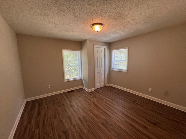 unfurnished bedroom with multiple windows, dark hardwood / wood-style floors, a textured ceiling, and a closet