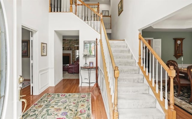 staircase featuring ornamental molding, a fireplace, wood finished floors, and a towering ceiling