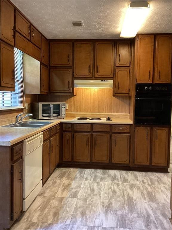 kitchen with under cabinet range hood, white appliances, a sink, light countertops, and brown cabinetry