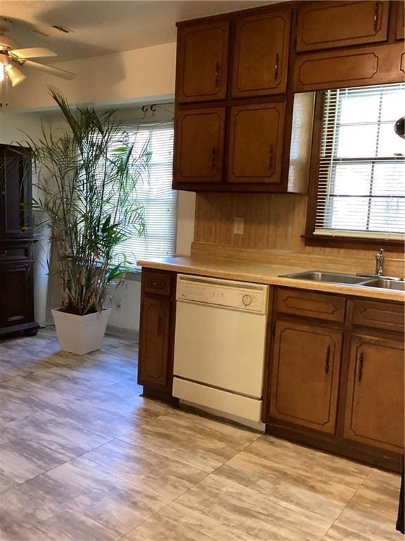 kitchen with white dishwasher, a sink, a ceiling fan, light countertops, and brown cabinetry