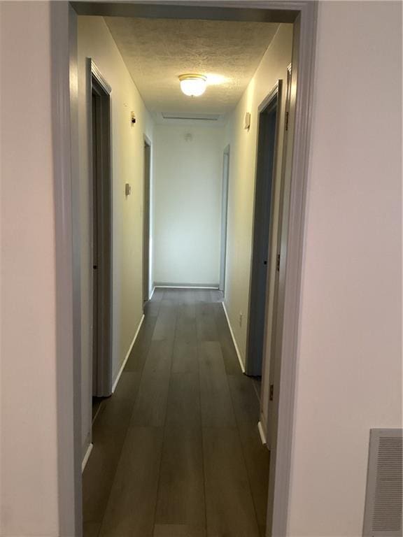 corridor with baseboards, visible vents, dark wood-style flooring, and a textured ceiling