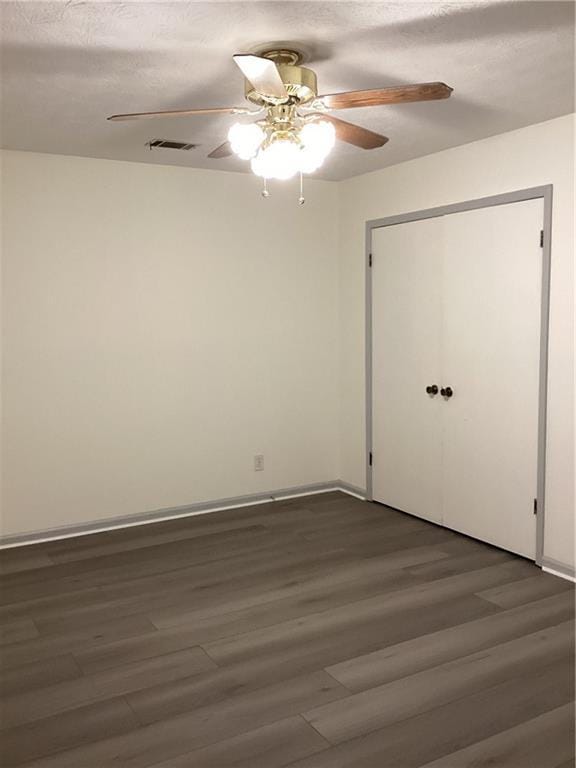 empty room featuring dark wood-style flooring, visible vents, ceiling fan, and baseboards