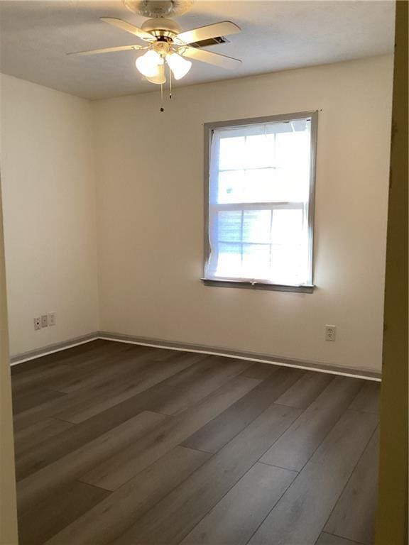 spare room featuring dark wood-style flooring, a ceiling fan, and baseboards