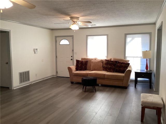 living room with visible vents, a ceiling fan, dark wood-style floors, a textured ceiling, and crown molding