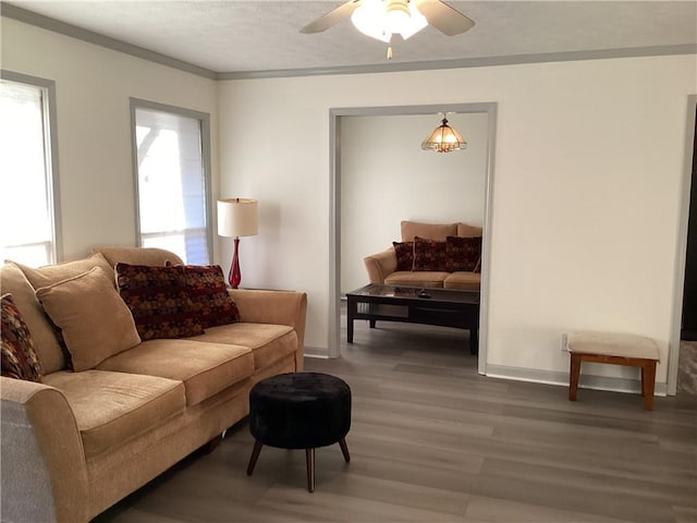 living room featuring a ceiling fan, crown molding, baseboards, and wood finished floors