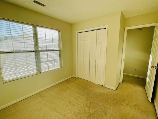 unfurnished bedroom featuring baseboards, visible vents, a closet, a textured ceiling, and light carpet