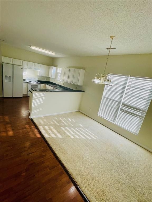 kitchen featuring dark countertops, white cabinetry, white appliances, a peninsula, and a chandelier