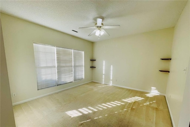 carpeted spare room with baseboards, visible vents, a textured ceiling, and a ceiling fan