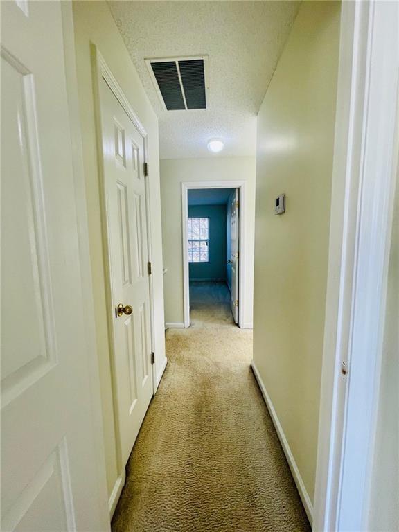 hallway with visible vents, baseboards, light colored carpet, and a textured ceiling