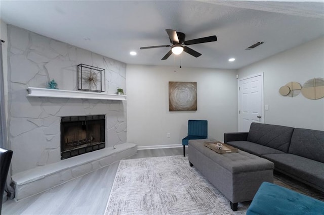 living room featuring wood-type flooring, a stone fireplace, and ceiling fan