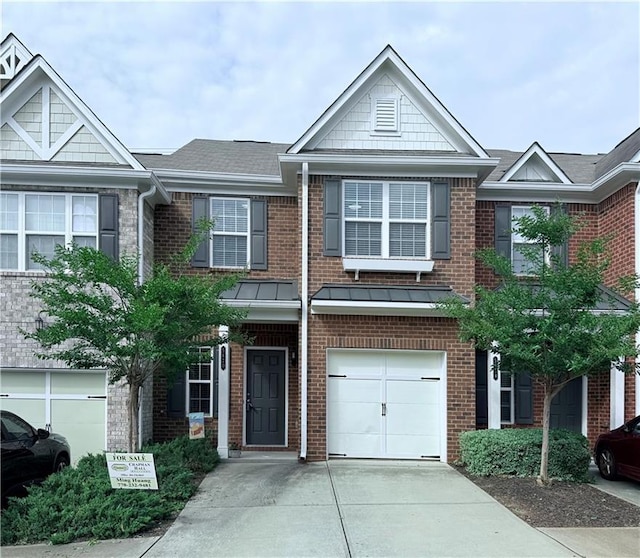 townhome / multi-family property with brick siding, a garage, concrete driveway, a shingled roof, and a standing seam roof