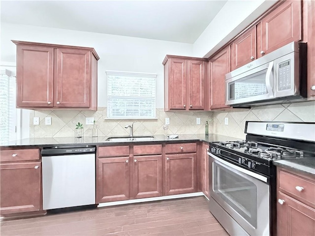 kitchen with stainless steel appliances, a sink, light wood-type flooring, and backsplash