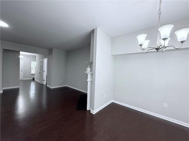 unfurnished room with wood finished floors, a chandelier, and baseboards