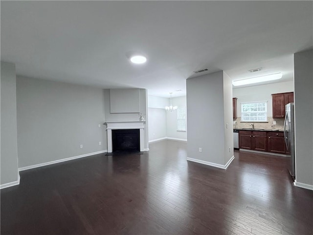 unfurnished living room with a sink, a chandelier, dark wood-style floors, a fireplace with flush hearth, and baseboards