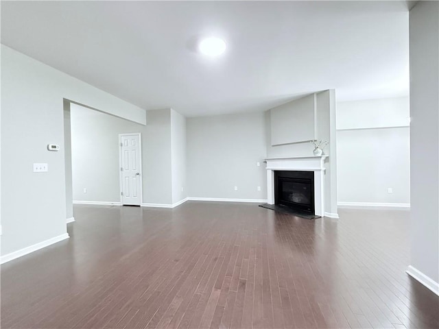 unfurnished living room featuring dark wood-style floors, a glass covered fireplace, and baseboards