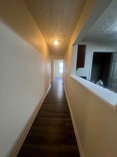 hall featuring baseboards, a textured ceiling, and dark wood-type flooring