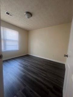 empty room with baseboards, dark wood-style floors, a textured ceiling, and visible vents