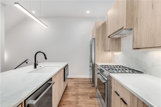 kitchen with sink, light brown cabinets, tasteful backsplash, light stone countertops, and appliances with stainless steel finishes