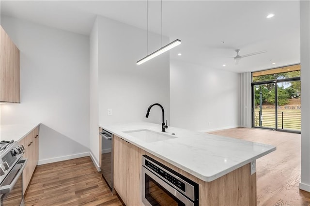 kitchen featuring light hardwood / wood-style floors, stainless steel appliances, kitchen peninsula, light brown cabinets, and sink