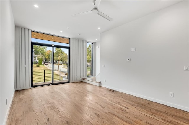 empty room with floor to ceiling windows, ceiling fan, and light hardwood / wood-style floors