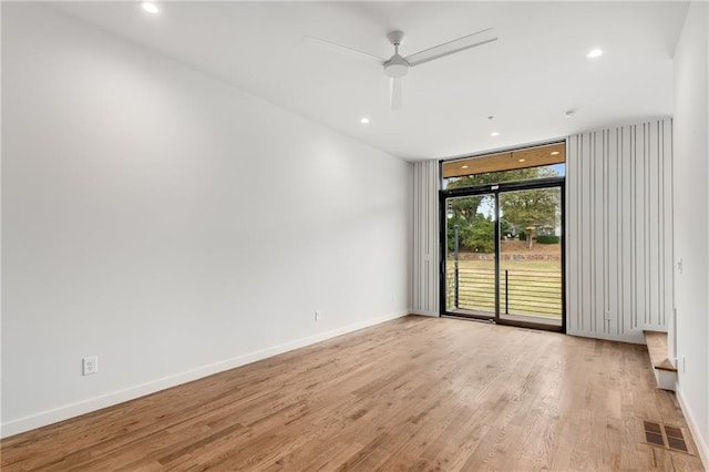 empty room with floor to ceiling windows, ceiling fan, and light hardwood / wood-style floors