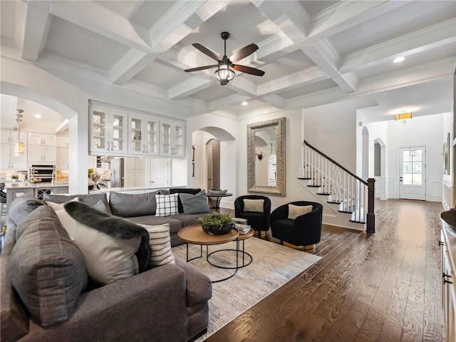 living room featuring dark wood-type flooring, beamed ceiling, ornamental molding, ceiling fan, and coffered ceiling