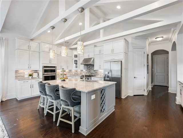 kitchen with appliances with stainless steel finishes, pendant lighting, white cabinets, and a kitchen island with sink