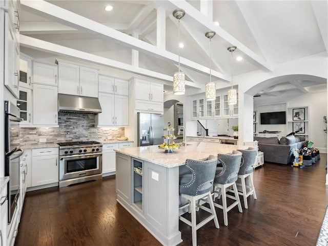 kitchen with appliances with stainless steel finishes, hanging light fixtures, an island with sink, light stone counters, and white cabinetry