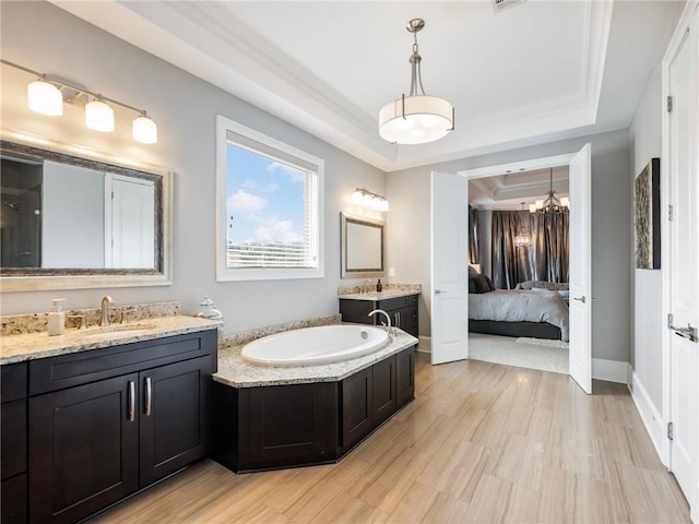 bathroom with a notable chandelier, a raised ceiling, hardwood / wood-style flooring, vanity, and crown molding