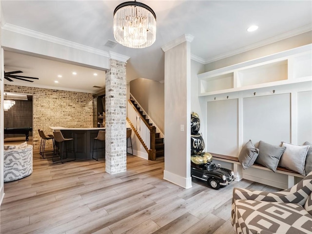 living room with brick wall, light wood-type flooring, decorative columns, and crown molding