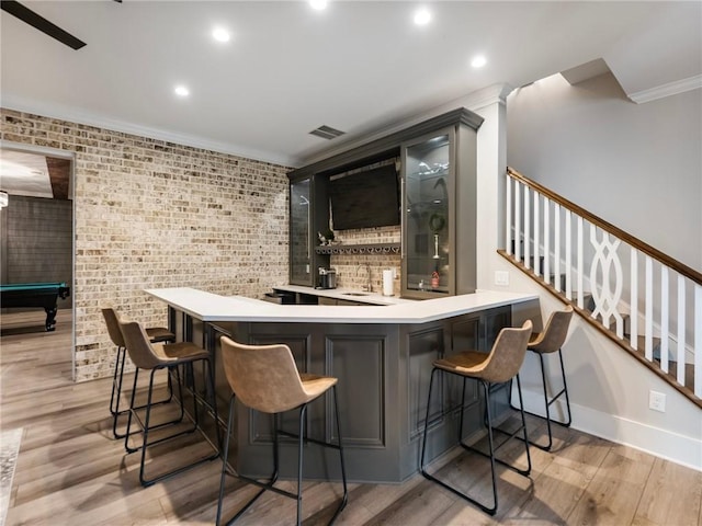 bar with pool table, brick wall, ornamental molding, sink, and light hardwood / wood-style flooring