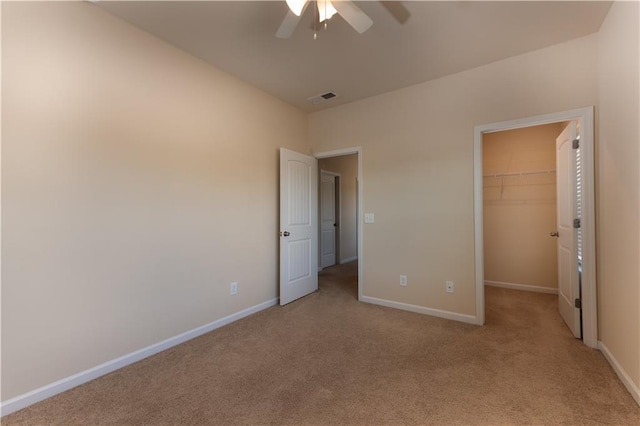 unfurnished bedroom with a walk in closet, a closet, ceiling fan, and light colored carpet