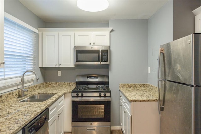 kitchen with white cabinets, appliances with stainless steel finishes, light stone countertops, and sink