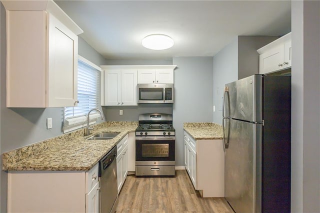 kitchen with light stone countertops, white cabinetry, sink, light hardwood / wood-style floors, and appliances with stainless steel finishes