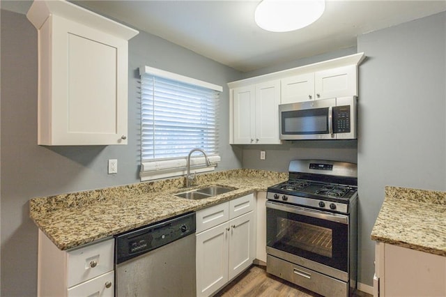 kitchen featuring white cabinets, appliances with stainless steel finishes, light stone counters, and sink