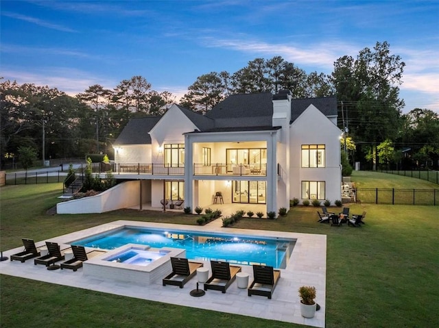 back house at dusk featuring a lawn, a balcony, a swimming pool with hot tub, and a patio area