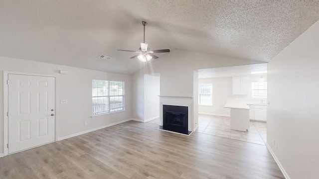 unfurnished living room featuring a ceiling fan, plenty of natural light, lofted ceiling, a textured ceiling, and a fireplace